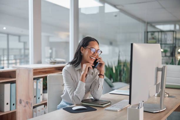 Kvinde på kontor taler i telefon foran computeren.