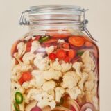 Glaskrukke med blomkål, gulerødder, løg og chili til syltning